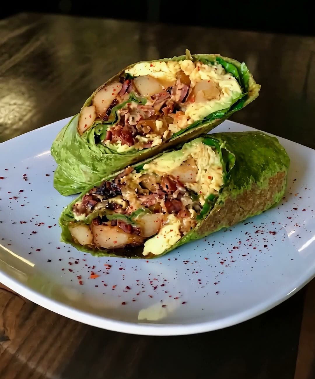 The Fully Loaded Burrito sliced in half on a white plate, layers of egg, beef bacon, potato, spinach and avocado visible in the cross-section.